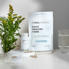Thera Nordic Daily Healthy Fibre packaging on a white surface with a plant and glass of water in the background.
