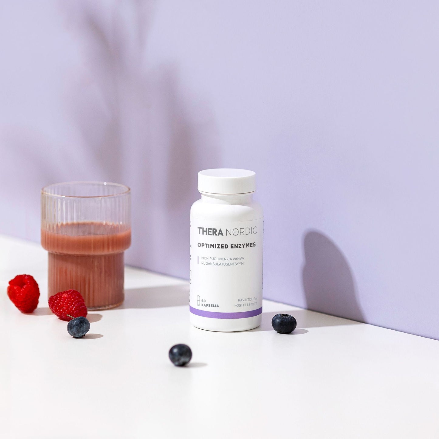 A white bottle of THERA Nordic Optimized Enzymes stands on a white surface next to a glass of pink liquid, with raspberries and blueberries nearby, suggesting digestive enzyme relief against a light purple background.