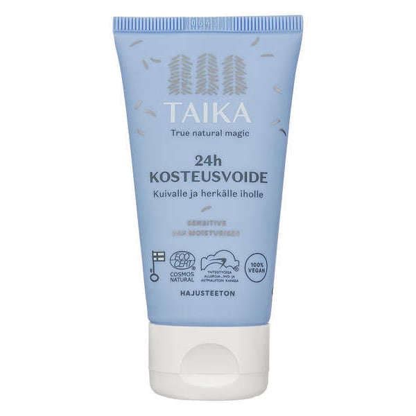 Auf der blauen Tube mit der Aufschrift Taika Sensitive 24h Moisturiser steht in finnischer Sprache, dass es sich um eine parfümfreie Feuchtigkeitscreme für trockene, empfindliche Haut handelt. Das Design enthält Blattillustrationen und Symbole für vegane/natürliche Zertifizierung.