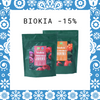Two green pouches of Biokia berry powder mixes are shown, with images of berries on the front. Text above them reads BIOKIA -15%. Blue and white floral border surrounds the image.