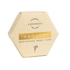 A hexagonal, cream-colored Luonkos box with gold accents and simple black text, featuring a botanical illustration. The Innocent Nurturing Body Cake is crafted by Luonkos with natural ingredients for dry and sensitive skin.
