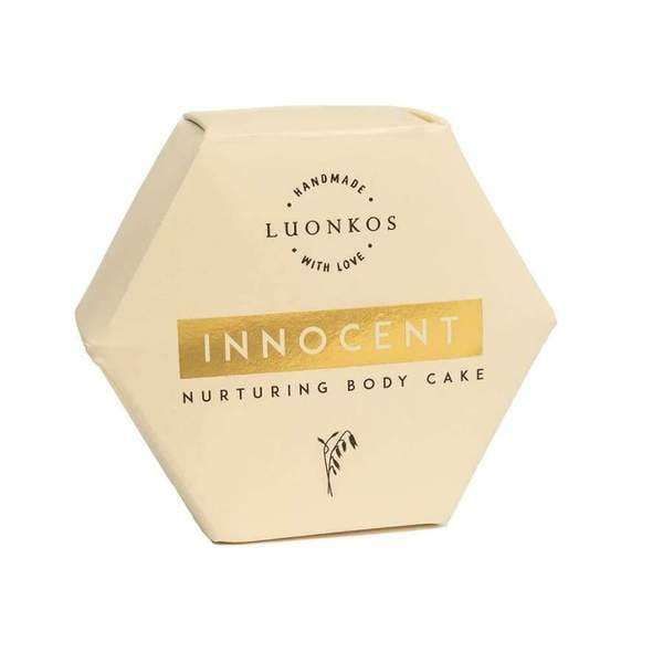 A hexagonal, cream-colored Luonkos box with gold accents and simple black text, featuring a botanical illustration. The Innocent Nurturing Body Cake is crafted by Luonkos with natural ingredients for dry and sensitive skin.