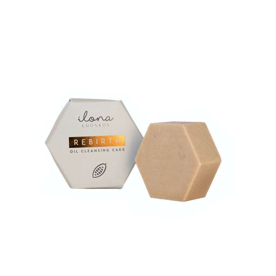 A hexagonal beige Luonkos Rebirth Oil Cleansing Cake rests next to its matching box labeled “Luonkos Rebirth Oil Cleansing Cake” with a cocoa bean graphic—a vegan, natural facial cleanser—against a white background.