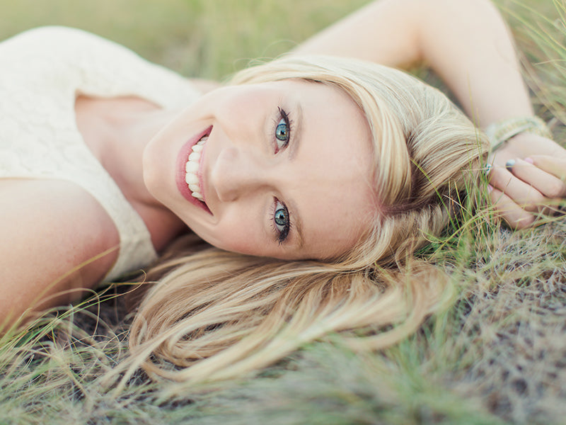 Blonde Frau mit blauen Augen lächelnd und auf Gras liegend