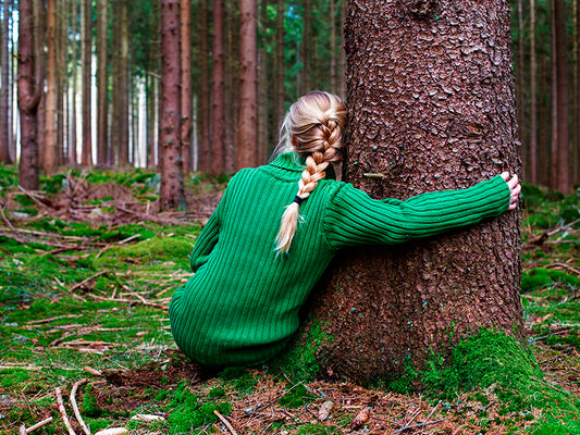 Eine Frau im grünen Pullover umarmt einen Baum im Wald