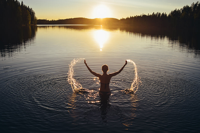 Eine Frau schwimmt in einem See in Finnland bei Sonnenuntergang