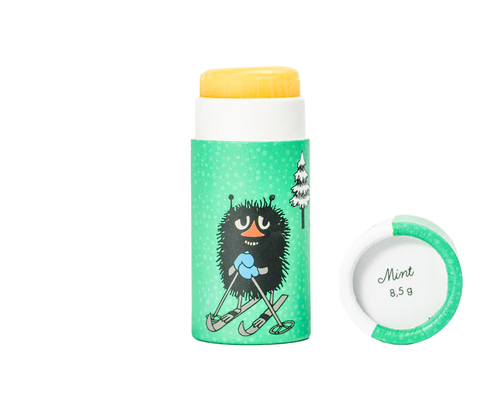 Der Gustaf & Linnea Mumin Lipbalm Stinki ist ein umweltfreundlicher Stift mit grüner Verpackung, zwei Baumillustrationen und der schwarzen Muminfigur Stinki auf Skiern. Hergestellt mit schwedischem Bienenwachs; auf der Kappe steht Mint 8,5 g.