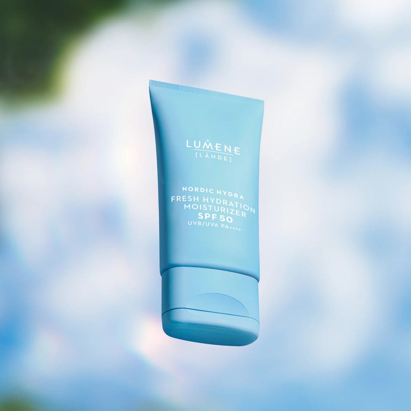 Eine blaue Tube Lumene Nordic Hydra Fresh Hydration Moisturizer SPF50 steht vor einem weichen, verschwommenen blauen und weißen Hintergrund, der einen frischen, luftigen Look erzeugt, der die tägliche Feuchtigkeitspflege von Lumene betont.