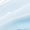 Eine glatte, hellblau-weiße, cremige Textur mit sanften Wellen und subtilen Rillen, wie Lumene Nordic Hydra Moisture Conditioner von Lumene, der auf einer Oberfläche verteilt wird.