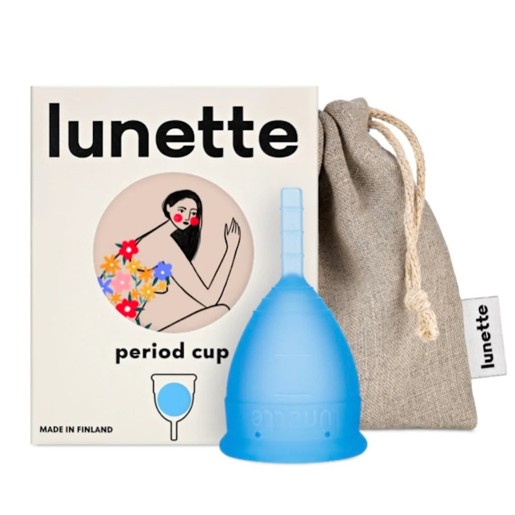 Eine blaue Lunette Menstruationstasse von Lunette liegt vor einer Markenschachtel mit einer illustrierten Frau und Blumen neben einem beigen Kordelbeutel mit der Aufschrift "Lunette" - einer umweltfreundlichen Menstruationslösung.