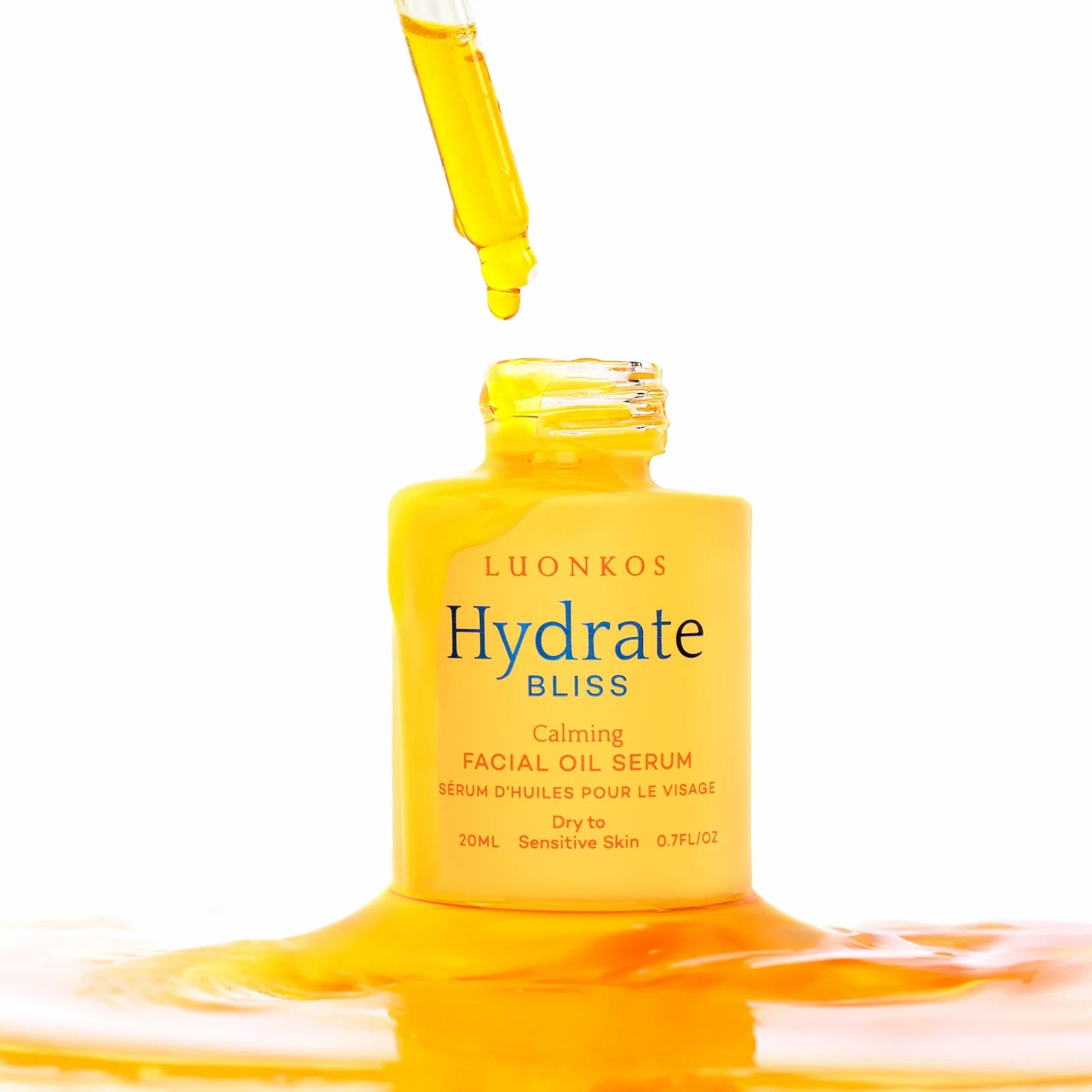 Ein Tropfer gibt gelbes Serum in eine offene gelbe Flasche mit der Aufschrift Luonkos Bliss Facial Oil Serum by Luonkos ab, umgeben von einer glänzenden Serumlache auf weißem Hintergrund.