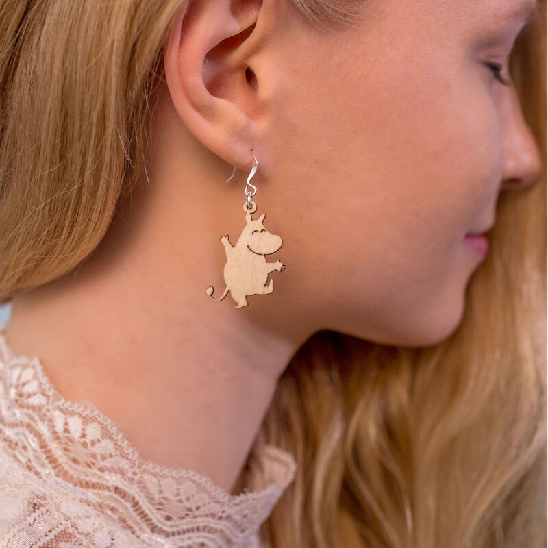 Eine Frau mit langem blondem Haar trägt ein Spitzenoberteil und leichte Holzohrringe in Form von Zeichentrick-Tieren - und zeigt damit die verspielten Coruu Moomin Wooden Earrings, die von nordischem Schmuck inspiriert sind.