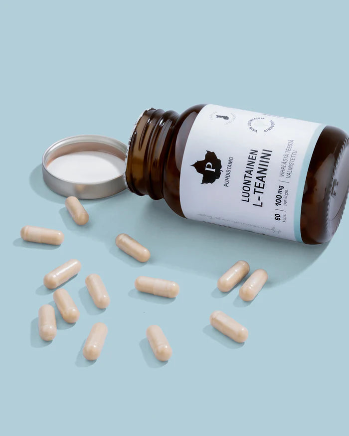 Eine braune Flasche mit der Aufschrift Puhdistamo Natural L-Theanine by Puhdistamo liegt ohne Deckel auf der Seite und verschüttet beigefarbene L-Theanin-Kapseln auf eine hellblaue Oberfläche, die ein Gefühl von Ruhe und Stressabbau hervorruft.
