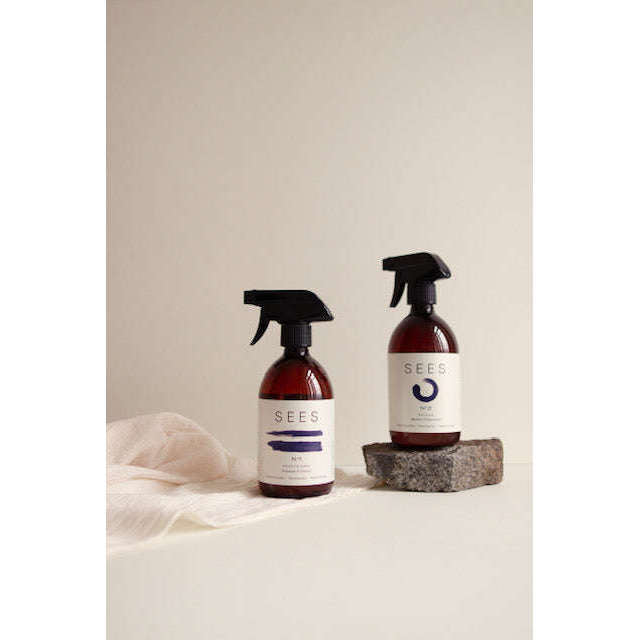 Zwei Flaschen SEES Company Textile Spray No. 2 Fresh, Orange & Peppermint ruhen auf einer hellen Fläche - eine auf einem Stein, die andere neben einem weichen Tuch. Die biologisch abbaubaren Sprays mit ätherischen Ölen werden vor einem schlichten, neutralen Hintergrund präsentiert.