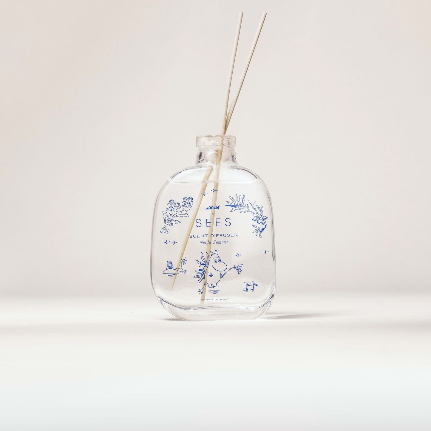 Die SEES Company x Moomin Room Diffuser Nordic Summer bietet einen aromatischen Duft in einer klaren Glasflasche mit blauen Blumenmustern und zwei dünnen Schilfstäbchen, präsentiert vor einem schlichten hellen Hintergrund.