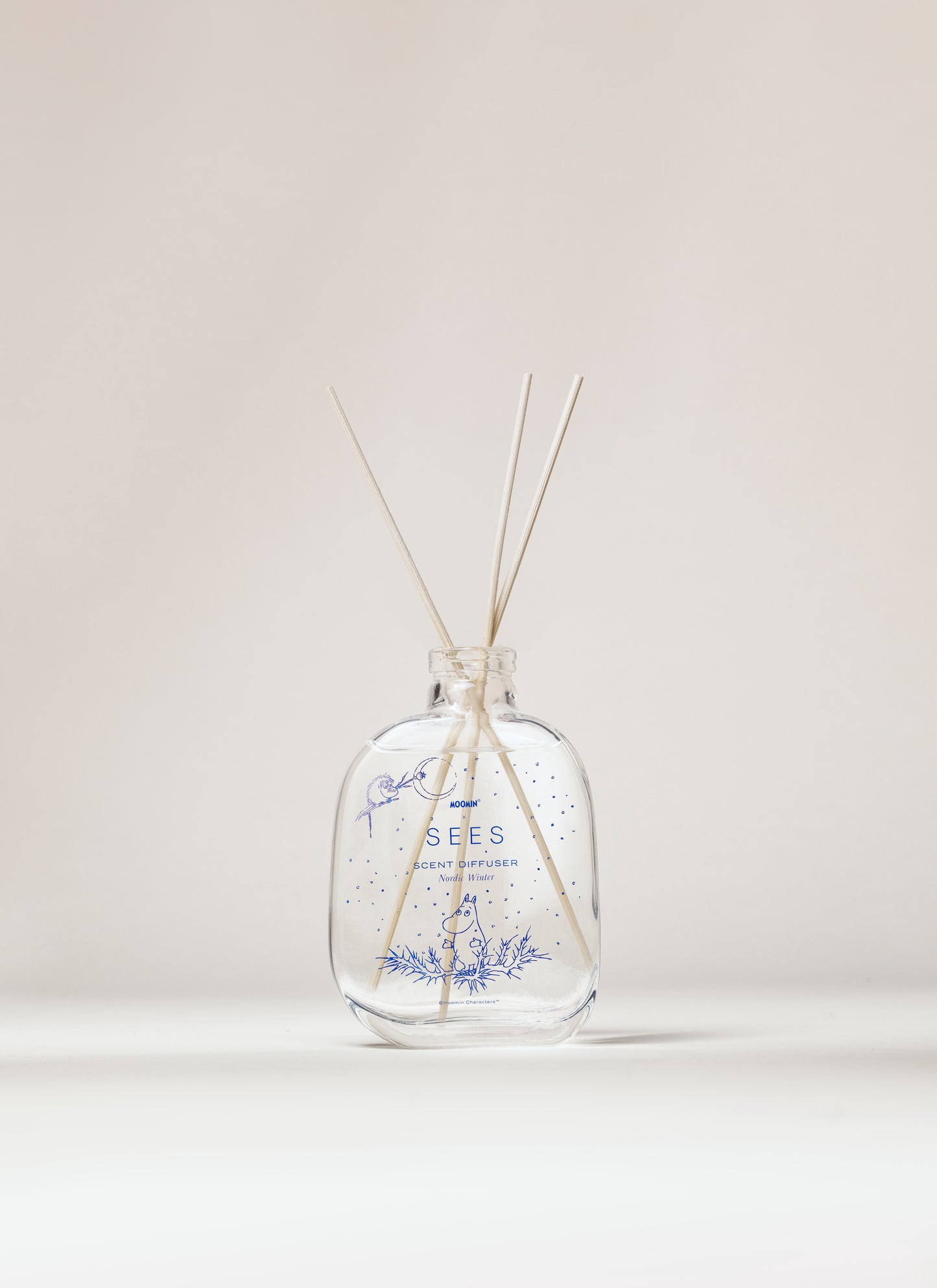 Der Raumduft „Nordic Winter“ von SEES x Moomin Room Diffuser Nordic Winter SEES Company einer klaren Glasflasche mit blauen Pflanzenstoffen und Holzstäbchen, die das finnische Design widerspiegeln, und präsentiert sich elegant vor einem neutralen Hintergrund.
