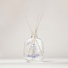 Der Raumduft „Nordic Winter“ von SEES x Moomin Room Diffuser Nordic Winter SEES Company einer klaren Glasflasche mit blauen Pflanzenstoffen und Holzstäbchen, die das finnische Design widerspiegeln, und präsentiert sich elegant vor einem neutralen Hintergrund.