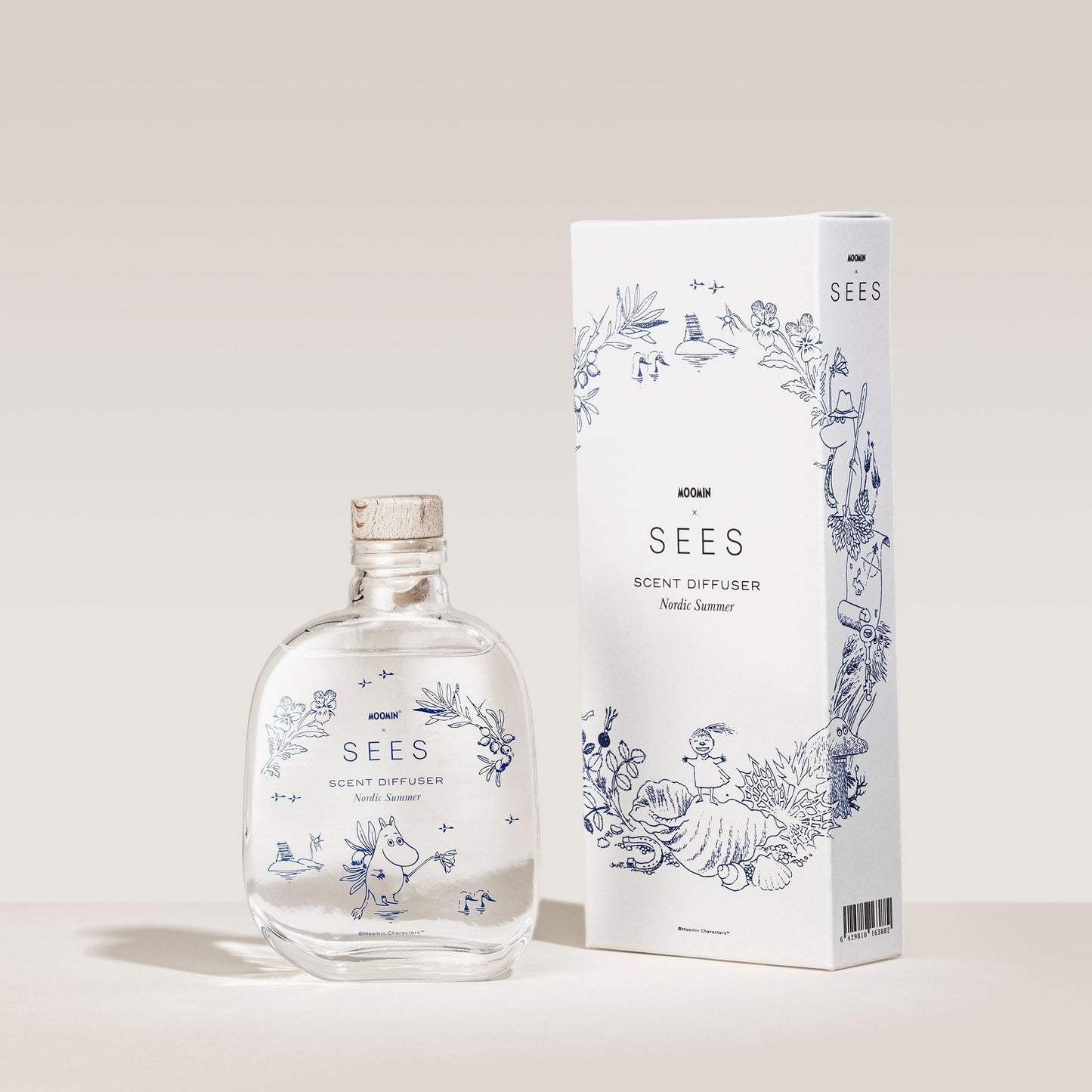 Die SEES Company x Moomin Room Diffuser Nordic Summer, ein biologisch abbaubarer Diffusor in einer klaren Glasflasche mit Korkverschluss, steht neben einer weißen Schachtel, die mit blauen Pflanzenmotiven und dem Markenlogo verziert ist – und erinnert an einen erfrischenden nordischen Sommerduft.