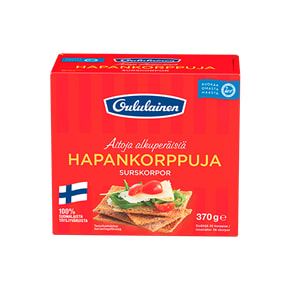 Une boîte rouge de pain croustillant Oululainen, fabriqué par Oululainen, présente une photo de pain croustillant au seigle complet avec du fromage, du concombre, de la tomate et des herbes. Un petit drapeau finlandais apparaît dans le coin inférieur gauche. Riche en fibres.