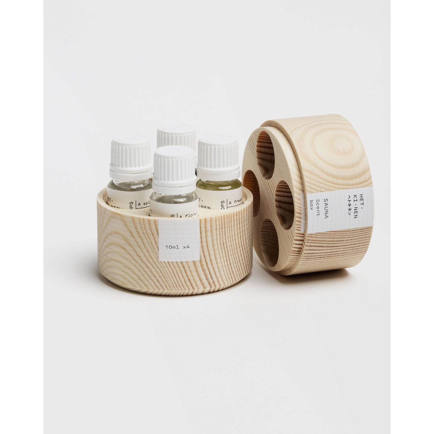 Quatre petites bouteilles de parfum pour sauna Hetkinen Sauna Scent Woody de Hetkinen avec bouchons blancs sont disposées dans un support rond en bois avec couvercle assorti, idéal pour une expérience authentique du sauna finlandais.