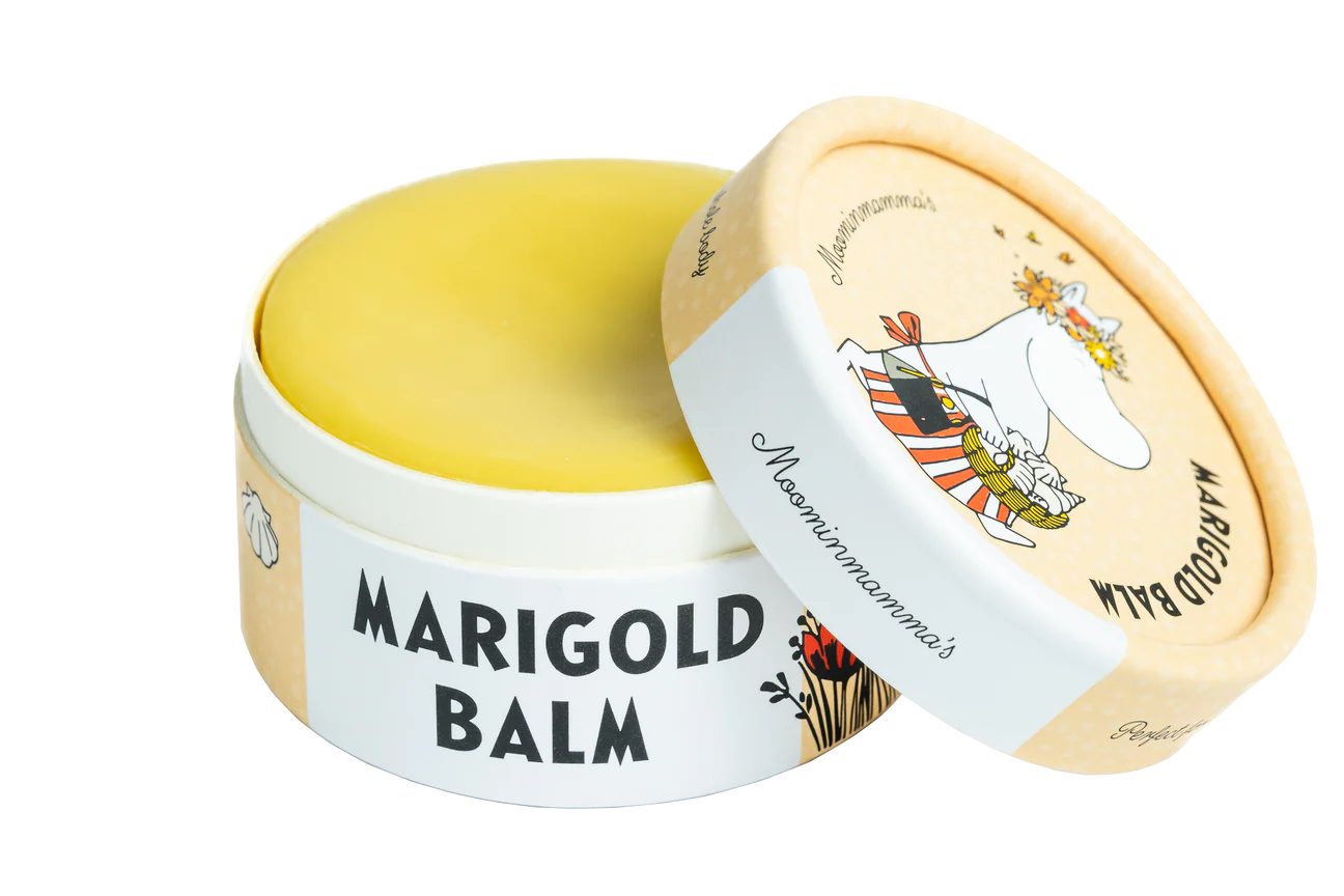 Un contenitore rotondo di Gustaf & Linnea Moominmammas Marigold Balm con il coperchio parzialmente aperto mostra un personaggio Moomin con una corona di fiori e una sciarpa a strisce. Il balsamo naturale giallo per la pelle è contenuto in una confezione ecologica Gustaf & Linnea.