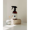 Una bottiglia spray marrone di detergente vegetale per cucina e bagno SEES Companyè appoggiata su un blocco di pietra accanto a un piccolo vaso bianco con fiori secchi, illuminato da una luce soffusa contro una parete chiara.