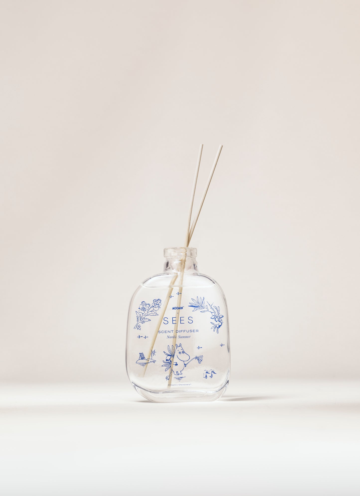 La SEES Company x Moomin Room Diffuser Nordic Summer presenta una fragranza aromatica in una bottiglia di vetro trasparente con motivi floreali blu e due sottili bastoncini di canna, presentati su uno sfondo semplice e chiaro.