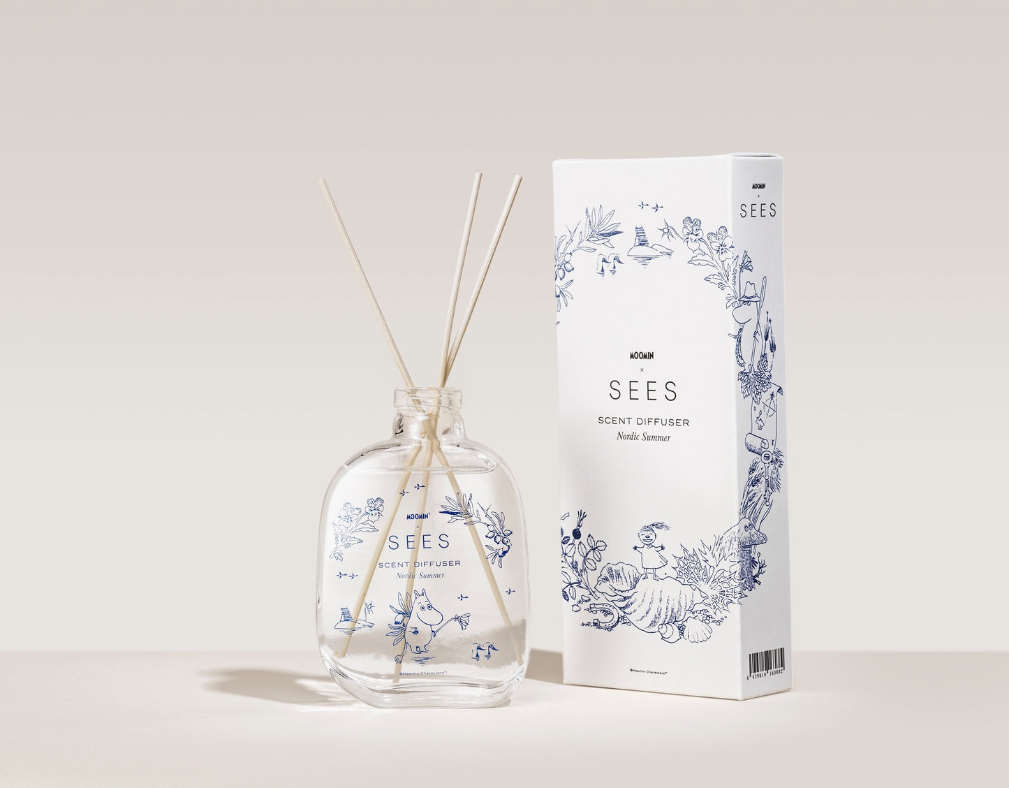 The SEES Company x Moomin Room Diffuser Nordic Summer, in una bottiglia di vetro trasparente con bastoncini di legno e una scatola bianca decorata con motivi floreali blu, cattura la fresca essenza dell'estate nordica su uno sfondo neutro.