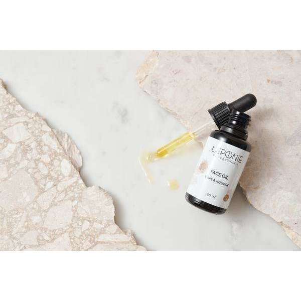 Una bottiglia di olio Laponie of Scandinavia con contagocce, pensata per pelli sensibili, poggia su una superficie di marmo con alcune gocce di olio versate. Sullo sfondo si intravedono leggere texture di pietra.