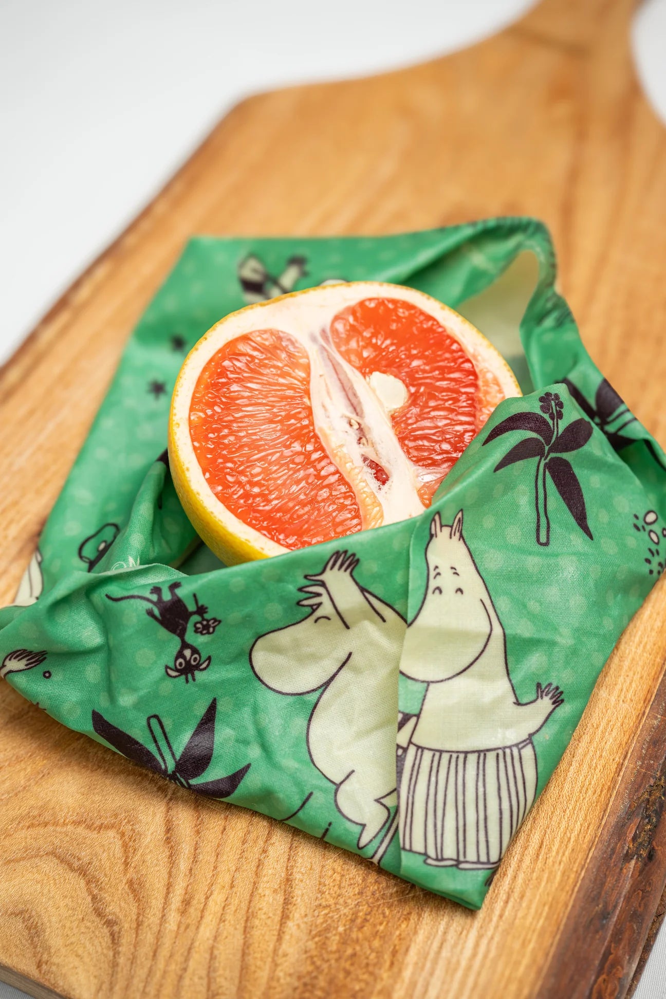 Een gehalveerde grapefruit, verpakt in een Gustaf & Linnea Moomin-bijenwasvoedselverpakking, ligt op een houten snijplank.