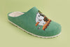 De Zapatillas Felt Slippers Snufkin zijn groene veganistische pantoffels met een witte pluizige voering, met Moomintroll en Snufkin op een oranje bank tegen een lichtgroene achtergrond. Duurzaam en charmant schoeisel voor fans.