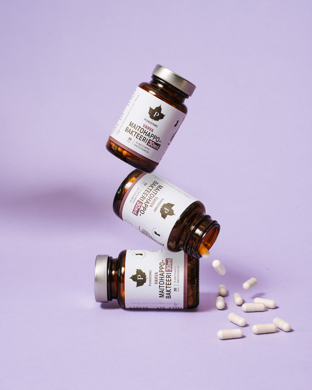 Drie flessen Puhdistamo Strong Probiotic 30 miljard CFU staan opgestapeld tegen een lichtpaarse achtergrond, met witte capsules ernaast – ideaal voor het ondersteunen van de darmgezondheid en immuniteit.
