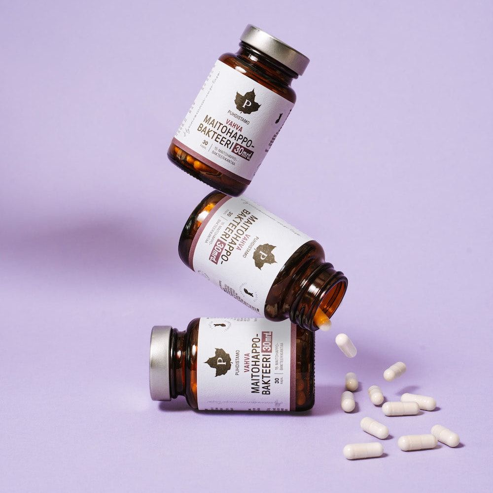 Drie flessen Puhdistamo Strong Probiotic 30 miljard CFU staan opgestapeld tegen een lichtpaarse achtergrond, met witte capsules ernaast – ideaal voor het ondersteunen van de darmgezondheid en immuniteit.