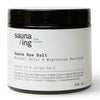 Een zwarte pot van 200 ml met Sauna Spa Salt van sauna/ing heeft een wit etiket met productinformatie en ingrediënten. Ideaal voor een ontgiftend bad of een ontspannend voetbad.