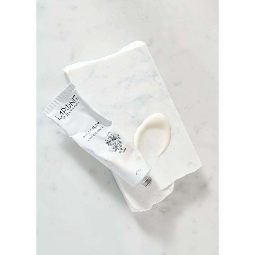 Een witte tube Laponie of Scandinavia Cream ligt op perkament naast een beetje crème, allemaal op licht marmer – een zachte formule van Laponie of Scandinavia de gevoelige huid.