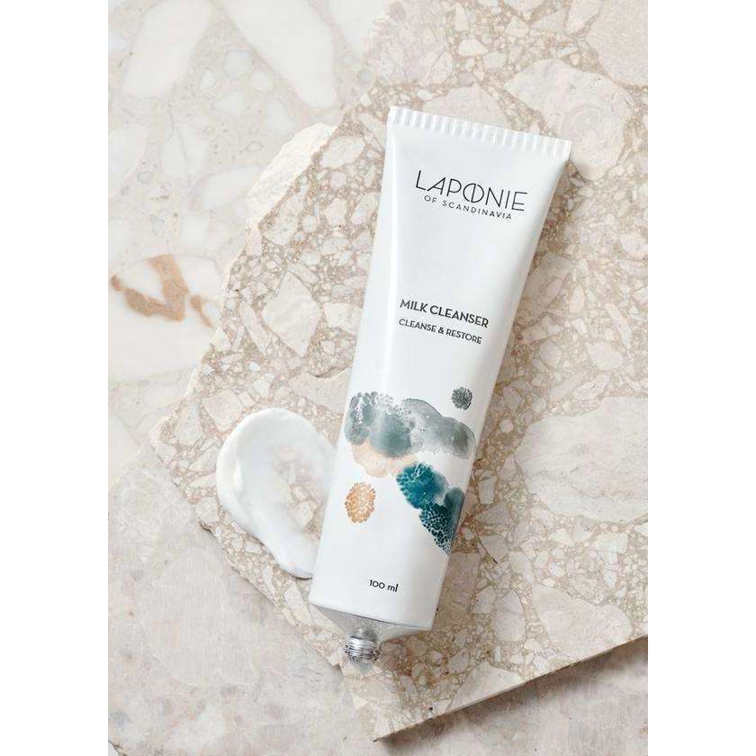 Een tube Laponie of Scandinavia Cleanser ligt op marmer, met een beetje van de milde formule ernaast. Op de tube van 100 ml staat abstracte kunst en tekst die aangeeft dat het een reinigingsmiddel voor de gevoelige huid is van Laponie of Scandinavia.