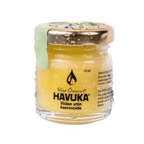 Een kleine glazen pot met gouden deksel met Havuka Five Herbs Facial Balm van Havuka. Deze gele Finse gezichts- en oogbalsem heeft een groen zegel en waterdruppels en is verrijkt met wilde kruiden uit Finland.