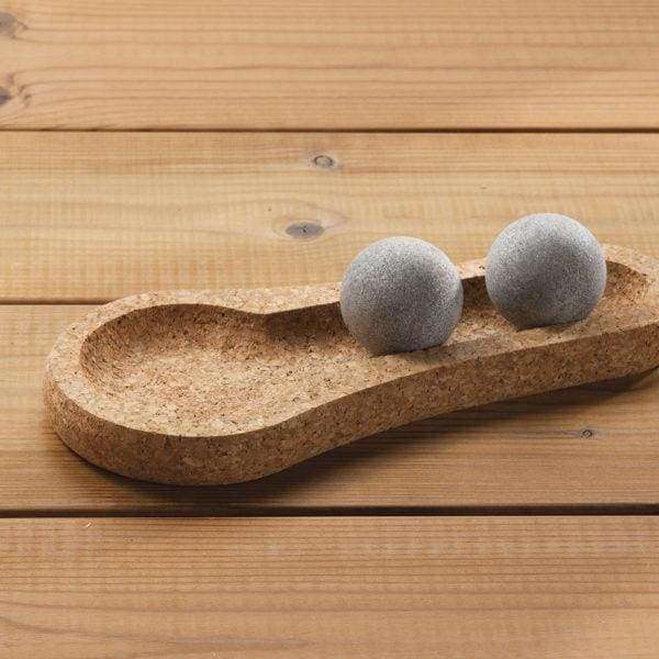 Twee gladde, grijze Hukka Solejoy-massageballen van Hukka staan op een voetafdrukvormige kurken voet, tentoongesteld op een houten oppervlak.